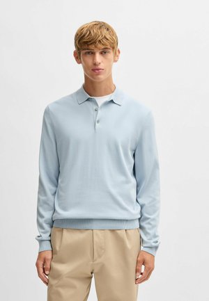 Polo a maniche lunghe azzurro chiaro con zip a tre bottoni, polsini e orlo a coste. Tessuto in maglia morbido. Abbinato a pantaloni beige.