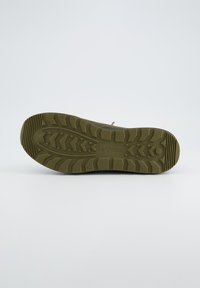 Semelle de sneaker vert olive avec une surface en caoutchouc texturée, présentant un motif en zigzag pour le traction et un logo embossé au centre.
