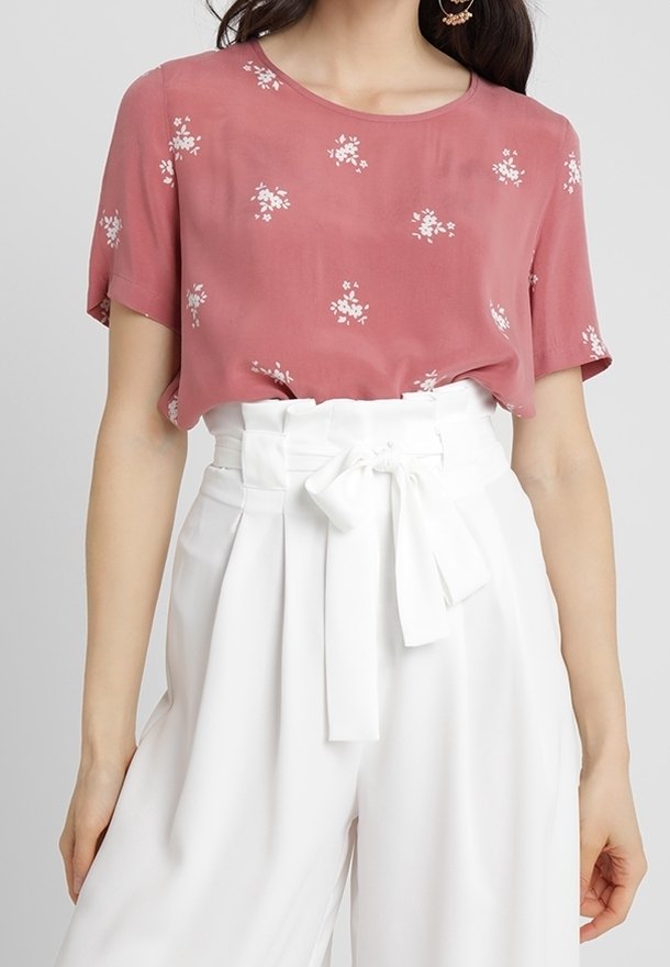Kort pink top med korte ærmer og hvidt blomstermønster, parret med højtaljede hvide bukser med en bundet sløjfedetalje.