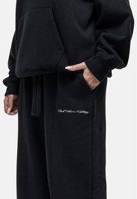 Zwarte sweater en joggingsbroek in een relaxte pasvorm, met een voorkantzak, een trekkoord en geborduurde tekst op het pijpje.