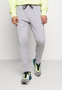 Ljusgråa träningsbyxor med dragsko i midjan, sidostripes och en åtsittande design, i kombination med färgglada löparskor med nätinslag.