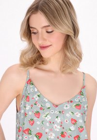 Top senza maniche verde chiaro con scollo a V e motivo floreale che presenta fragole rosse e fiori bianchi su un tessuto morbido.