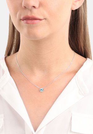 Collana d'argento con un piccolo pendente rotondo di gemma blu. La catena è delicata con un semplice design a maglie. Il pendente è incastonato in una montatura d'argento.