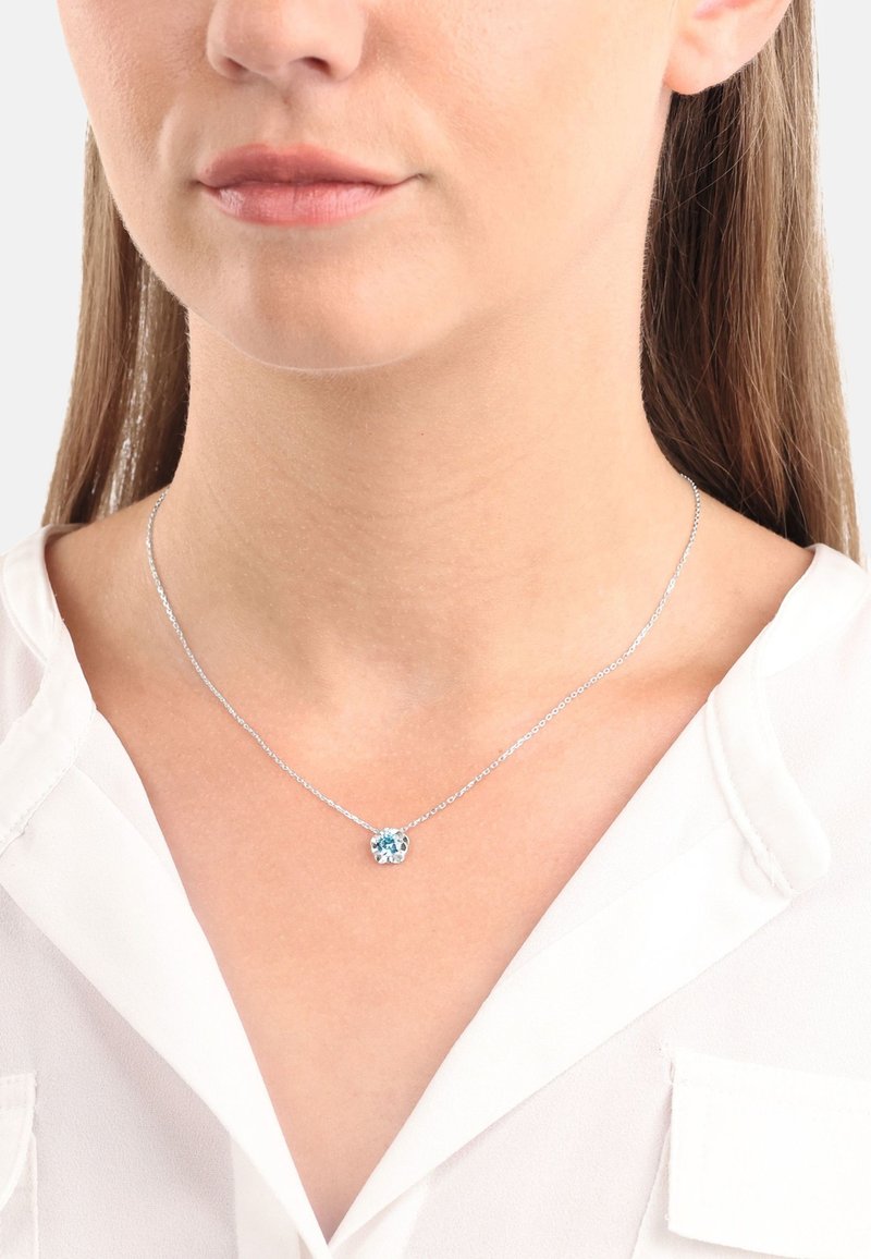 Silverhalsband med en liten, rund blå ädelsten pendel. Kedjan är delikat med en enkel länkdesign. Pendeln är inramad i en silverfattning.