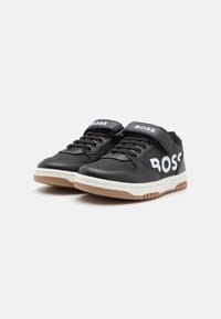 Schwarze Low-Top-Sneaker mit weißem "BOSS"-Logo, schwarzen Schnürsenkeln, Klettverschluss, weißer Zwischensohle und hellbrauner Gummisohle.