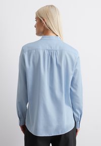 Light blue long-sleeve shirt made of smooth fabric. Back features a pleat for ease of movement. Buttoned cuffs and a classic collar.