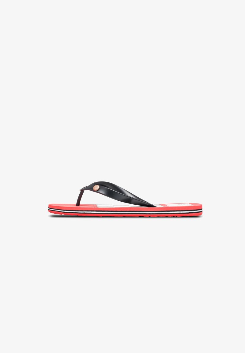 Chanclas de plástico negras con una suela roja que presenta rayas blancas y negras. Acento metálico circular notable en la correa.