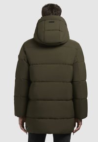 Olivengrøn pufferjakke med polstret design, justerbar hætte og lange ærmer. Har sidelommer og en let rundet kant.