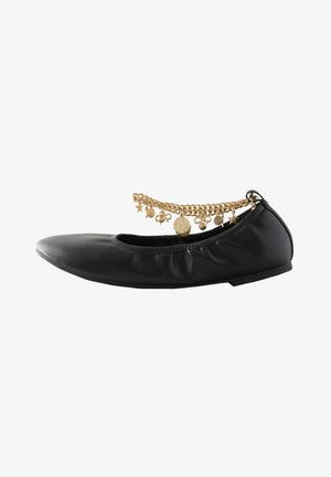 Chaussure plate noire en cuir froncé avec une bride de cheville en chaîne dorée ornée de breloques en forme d'étoile, de pièce et de nœud.