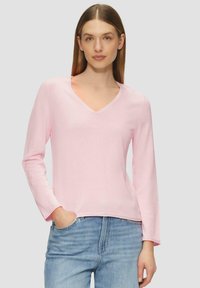 Helles rosafarbenes Langarmshirt mit V-Ausschnitt aus weichem Stoff, mit lockerer Passform und feinen Saumdetails. Kombiniert mit hellblauen Jeans.