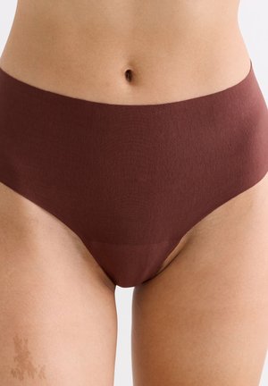 Nahaufnahme einer Person, die nahtlose, hoch taillierte braune Unterwäsche trägt, die den unteren Bauch und die oberen Oberschenkel vor einem neutralen Hintergrund zeigt.