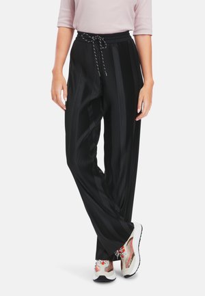 Schwarze, plissierte Hose mit elastischem Bund und Kordelzugdetails. Kombiniert mit bunten, klobigen Sneakers.
