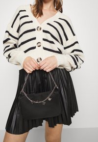 Knit cardigan med svarta ränder, stora knappar; veckad svart konstläderkjol; liten svart väska med kedja och fjärilsberlock.