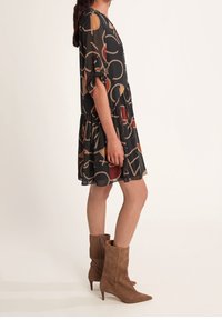Svart klänning med ett mönster av cirklar och repmotiv, korta ärmar och en utsvängd nederdel, i kombination med bruna högklackade stövlar.