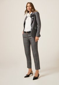 Completo grigio a quadri con accenti rossi, vestibilità sartoriale, giacca monopetto, camicia bianca, cintura nera e décolleté neri lucidi.
