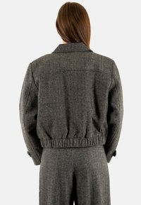 Grijze korte jas van een gestructureerde stof, met een grote kraag en een elastische tailleband. Voorzien van met knopen afsluitbare manchetten en een getailleerde pasvorm.