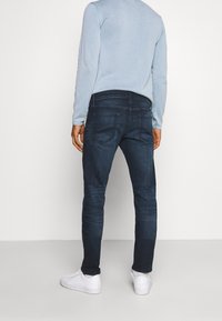 Mörkblå denimjeans med slim fit, med bakfickor, bärs med en ljusblå långärmad topp och vita sneakers.