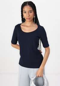 Μπλε νυχτερινό κοντομάνικο μπλουζάκι με στρογγυλή λαιμόκοψη και απαλή υφή, συνδυασμένο με ανοιχτό γκρι παντελόνι και ασημένια τσάντα.