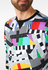 Buntes Sweatshirt mit geometrischen Mustern in Schwarz, Grau, Blau, Rot, Grün, Gelb und Lila sowie einem gerippten schwarzen Halskragen.