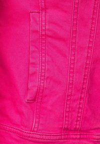 Pink denim jacket section featuring a flap pocket, visible stitching detail, and smooth texture. Bright color emphasizes the fabric's design.