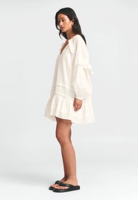 Valge volangidega kleit, millel on pikad varrukad ja kihiline alläär. Koos mustade plätudega, mida rõhutab pehme ja tekstuuriga kangas.
