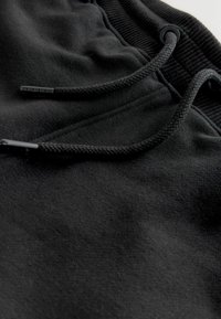 Schwarze Jogginghose mit glatter Textur, elastischem Bündchen und Kordelzug mit Aglets. Minimalistisches Design ohne sichtbare Muster.