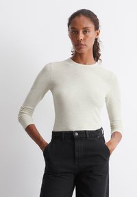 Lys grå, tettsittende langermet topp med rund hals, ribbet tekstur, sammen med høyt liv svarte jeans, hender i lommene.
