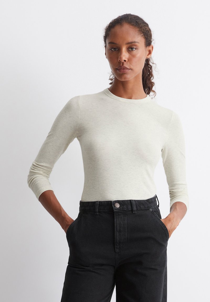 Lys grå, tettsittende langermet topp med rund hals, ribbet tekstur, sammen med høyt liv svarte jeans, hender i lommene.