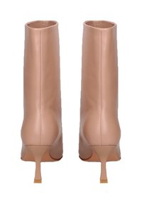 Un paio di stivali in pelle color nude con tacco a kitten appuntito, visti di spalle su sfondo bianco.