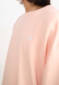 Ljusrosa sweatshirt med lös passform, med en liten vit Nike-logga på bröstet. Mjukt tyg med rund halsringning.