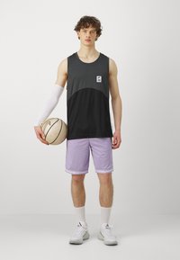 Sort og grå atletisk tanktop med et logo, parret med lilla shorts, hvid kompressionærme og hvide sneakers, mens der holdes en basketball.
