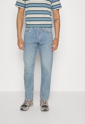 Jeans di denim di un azzurro chiaro con una vestibilità a gamba dritta, caratterizzati da cinque tasche e passanti per la cintura, abbinati a una maglietta a righe multicolore.