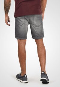 Shorts en denim gris avec des ourlets roulés, poches arrière et une texture délavée, associés à des baskets navy avec des accents blancs.