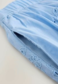 Tessuto di cotone azzurro con dettaglio arricciato e accenti di ricamo floreale. Texture liscia, con una lieve lucentezza e cuciture delicate.