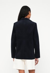 Mornarski sako od manšestera s izrezanim reverom, dugim rukavima i ravnim krojem. Stražnji dio ima središnji šav i minimalističke dizajnerske detalje.