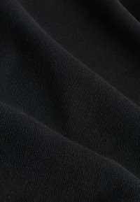 Tissu noir avec une texture côtelée, surface légèrement brillante, présentant des plis et des ombres qui mettent en valeur la profondeur de son matériau.