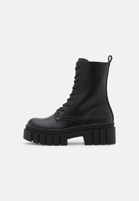 Black leather ankle boot with chunky, ridged sole, lace-up front, and pull tab on smooth white background.