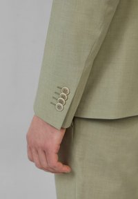 Manche d'une veste de costume vert clair présentant quatre boutons de couleur claire, texture lisse et coupe ajustée mettant en valeur des détails de couture subtils.