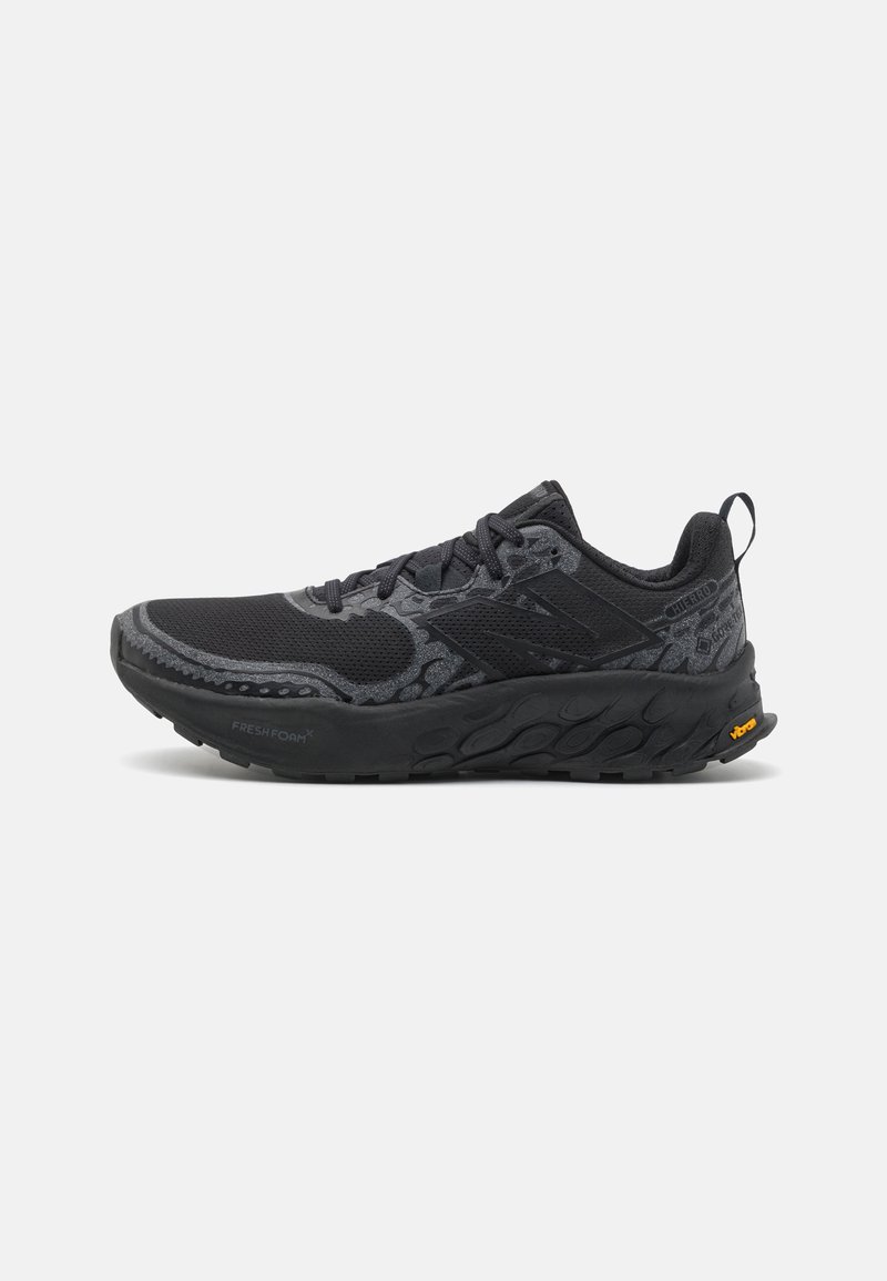 Black athletic shoe featuring a textured mesh upper, padded collar, and a robust sole. Includes logo accents and reflective detailing.