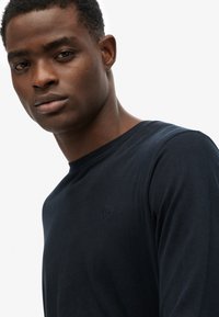 Navy blauwe katoenen T-shirt met lange mouwen en een ronde hals, met een klein geborduurd logo op de borst en een gladde, zachte textuur.