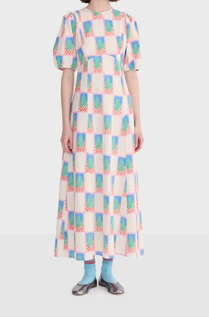 Mujer con un vestido largo de mangas abullonadas y un patrón geométrico colorido, combinado con calcetines azul claro y bailarinas metálicas.