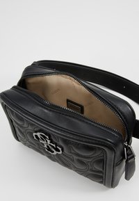 Czarna skórzana torebka na ramię z pikowanym wzorem, srebrnymi akcentami, zapięciem na zamek i beżowym wnętrzem z nadrukiem logo.