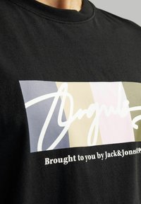 Camiseta de algodón negra con un gráfico colorido que presenta rayas en tonos pastel y texto en cursiva blanca. Cuello redondo y diseño de ajuste regular.