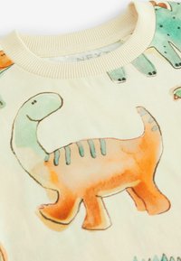 Hellbeige Sweatshirt mit bunten Dinosaurier-Illustrationen in Orange, Grün und Blau, einem gerippten Halsausschnitt und weichem Material.
