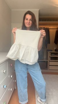 Cremfarbener Peplum-Top aus leichtem Stoff, mit raffiniertem Bund und weicher Textur. Kombiniert mit hellblauen, lässigen Jeans.