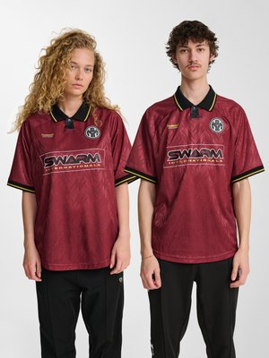 Dos modelos que llevan camisetas deportivas granate a juego con cuellos negros y el logo "Swarm Internationals", de pie frente a un fondo blanco liso.
