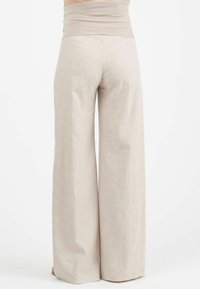 Weite Hosen aus einem hellbeigen Stoff mit einem glatten, dehnbaren Bund. Das Design zeigt eine fließende Silhouette und eine sanfte Textur.