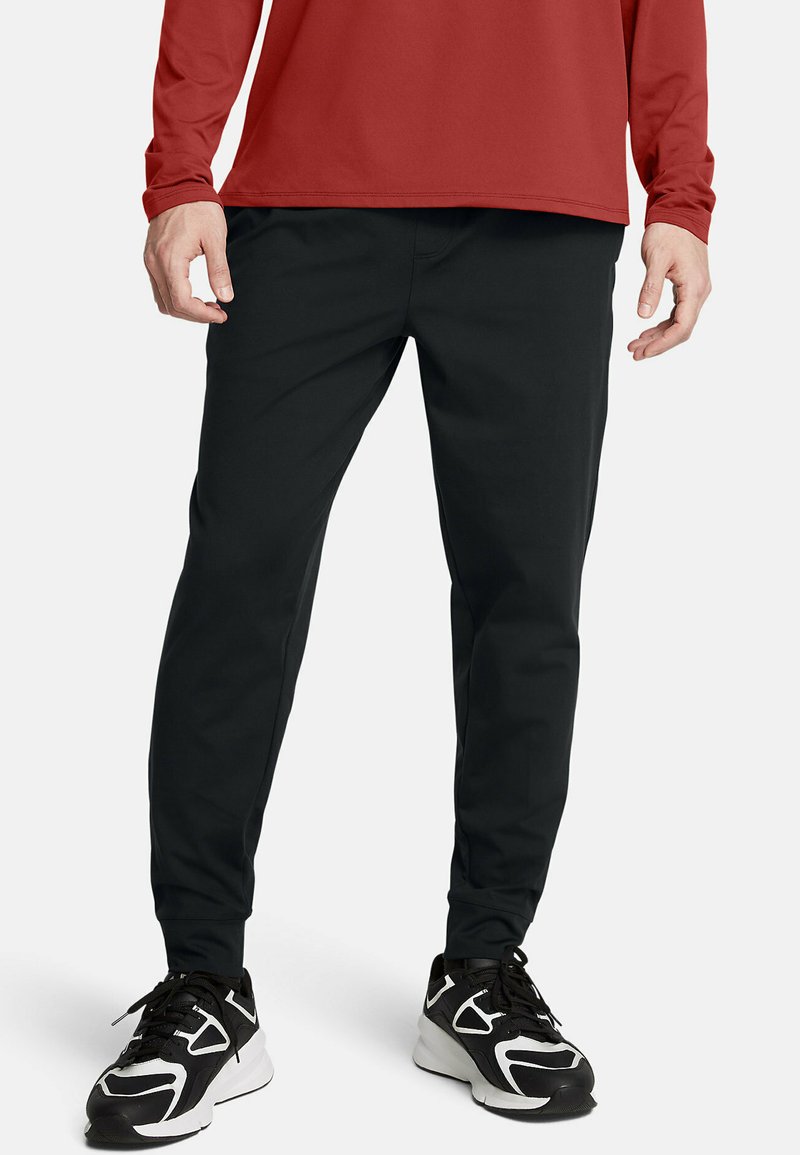 Zwarte taps toelopende broek gemaakt van een gladde, rekbare stof. Draag het met een rode langslang shirt en zwarte sport schoenen met witte accenten.