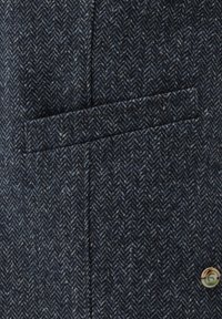 Dunkelblauer Fischgrätstoff mit kleiner Brusttasche und Knopfdetails. Die Textur ist gewebt und leicht grob.