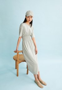 Light gray dress with a smocked waist, short sleeves, and flowy bottom; paired with a matching gray cap and beige slip-on shoes.